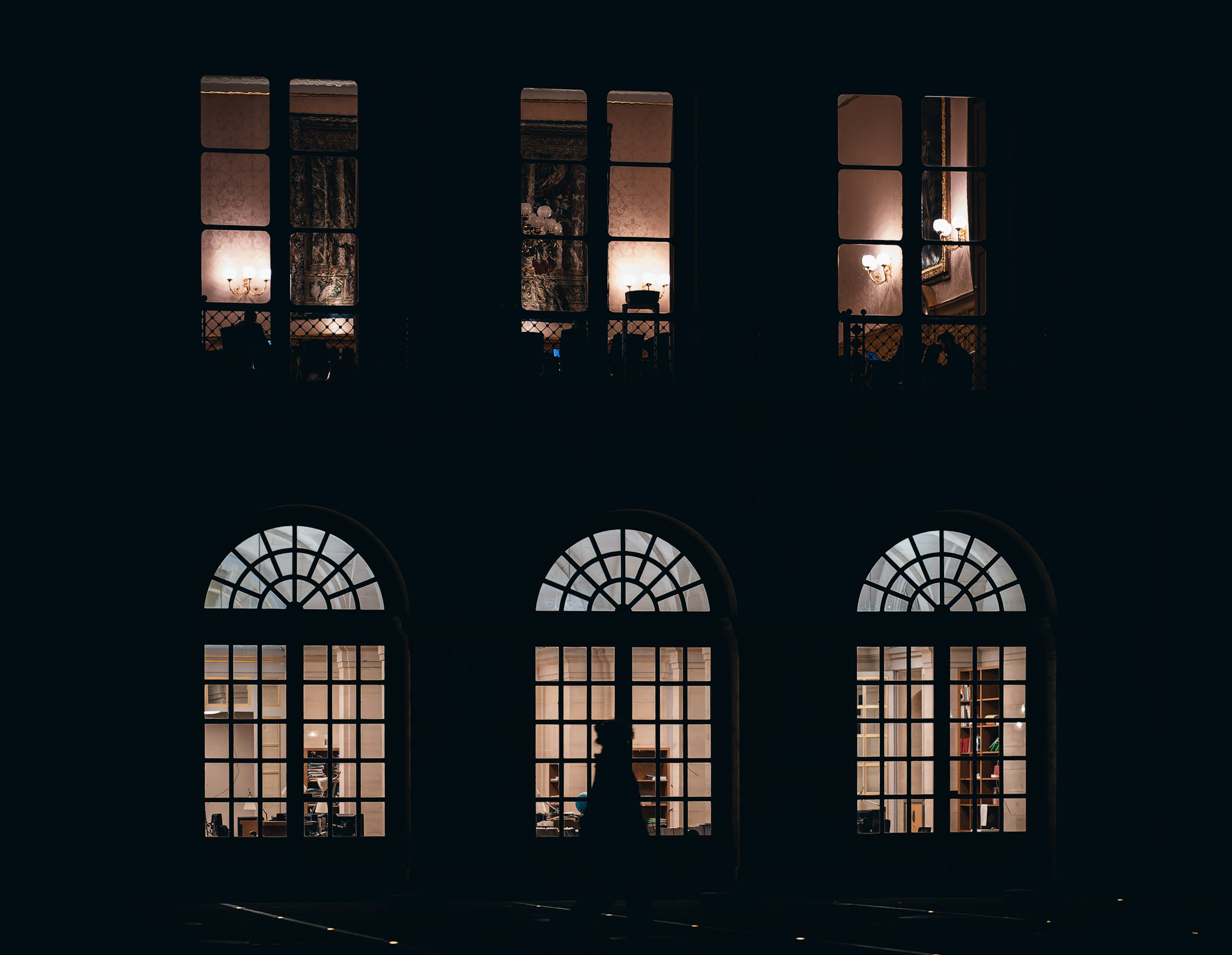 A dark stone facade at night with warm light in the windows